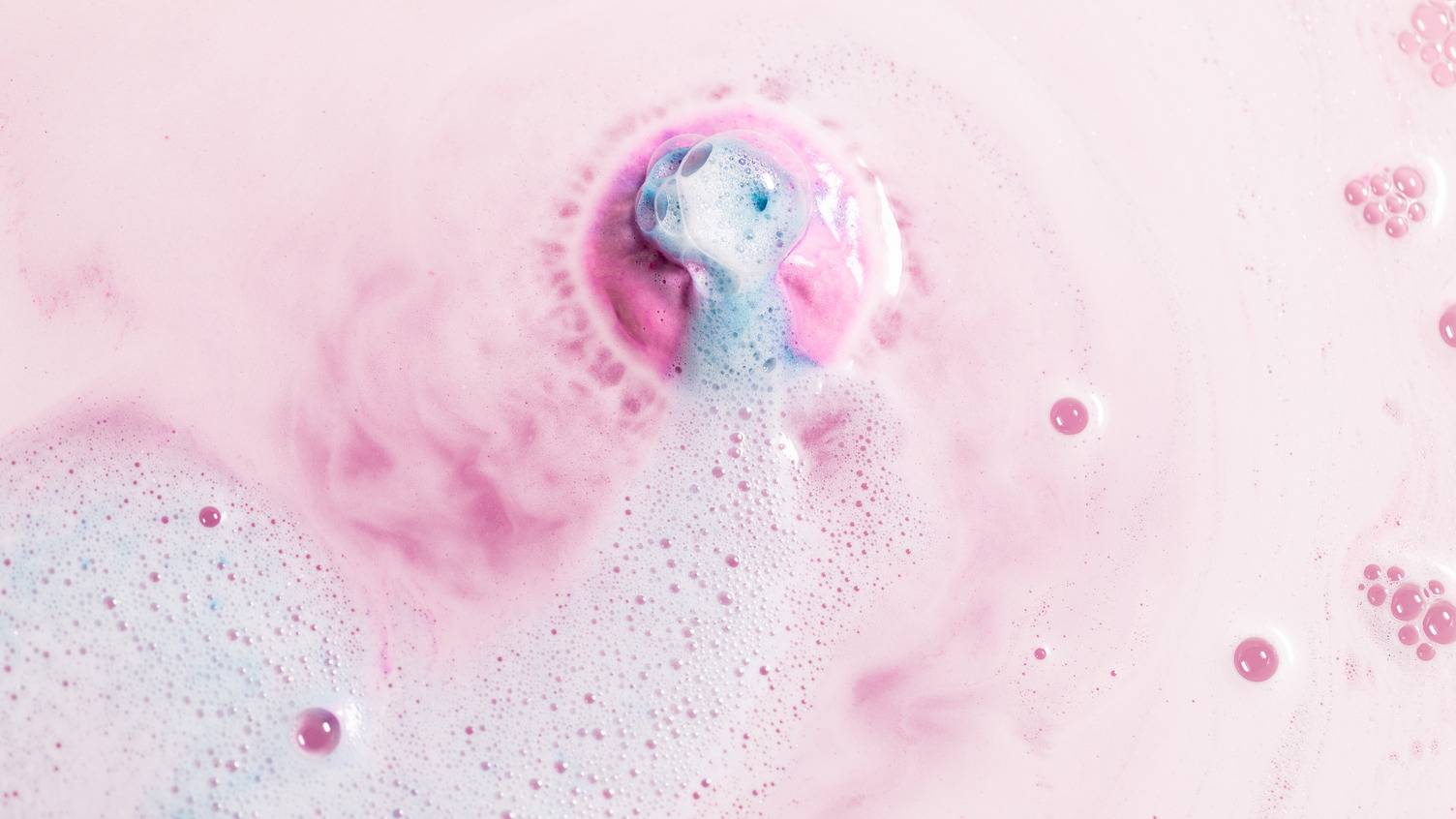 An aerial view of the Twilight bath bomb as it slowly dissolves. The bath has been covered in a blanket of thick, velvety, pastel pink foam as a flash of blue emerges from the centre of the product.